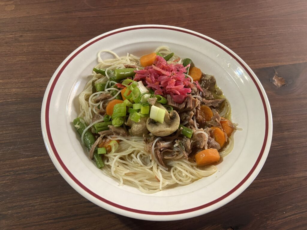 plate with homemade chicken noodle soup and vegetables on top, on a wooden table
