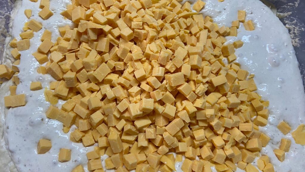 Sourdough bread dough in mixing process with sourdough starter and cheddar cheese on top.