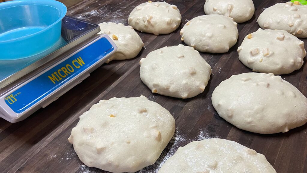 Sourdough bread dough with cheddar cheese pre-shaped into round balls on wooden table top.