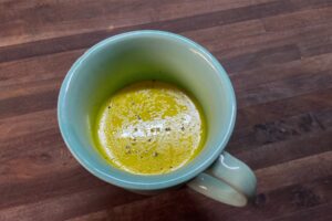 Spiced milk in green cup on wooden table with freshly grind black pepper on top