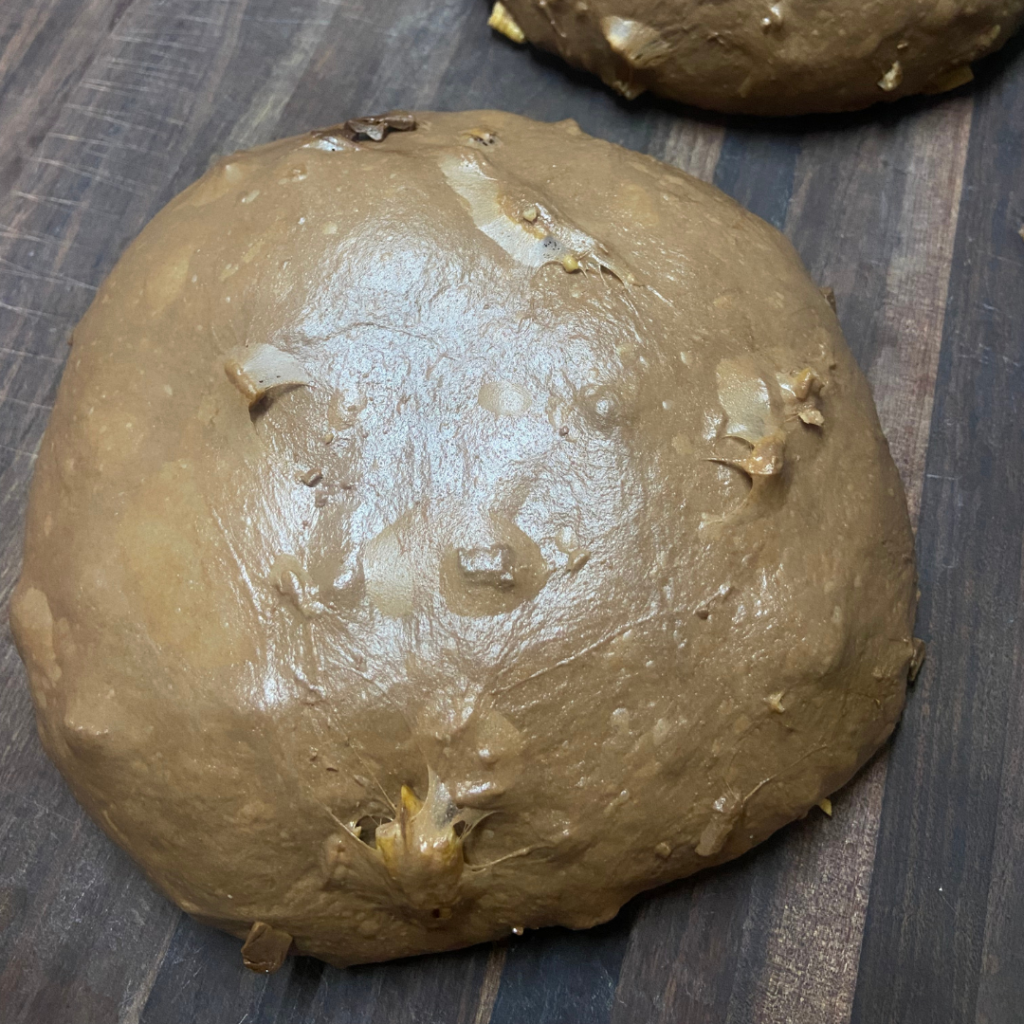 Chocolate dough on wooden table with chocolate and pecan pieces sticking out.